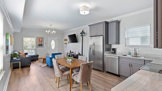 A modern kitchen with grey cabinets, a stainless steel refrigerator, and a dining area with a wooden table and chairs. - Modern 4BR Mid-City home with heated pool & parking. Steps to streetcar, near FQ & parades. (New Orleans)