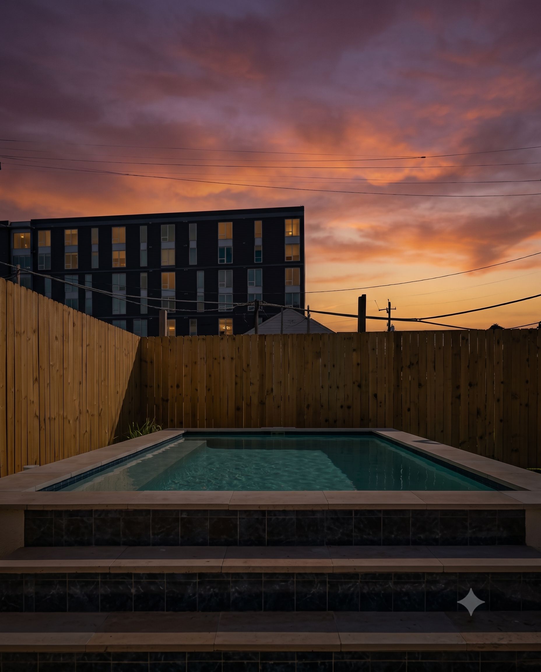 A swimming pool with a wooden fence and steps leading up to it, set against a sunset sky.