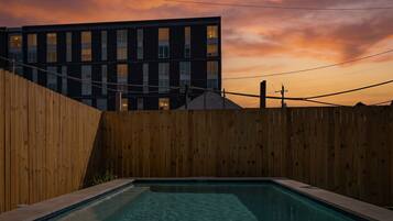 A swimming pool with a wooden fence and steps leading up to it, set against a sunset sky.