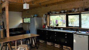 Una cocina rústica con vigas de madera, un refrigerador, un lavamanos y una ventana con vistas a un bosque.