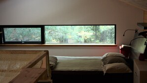 Una habitación pequeña con cama individual y un ventanal grande que ofrece vistas a un bosque.