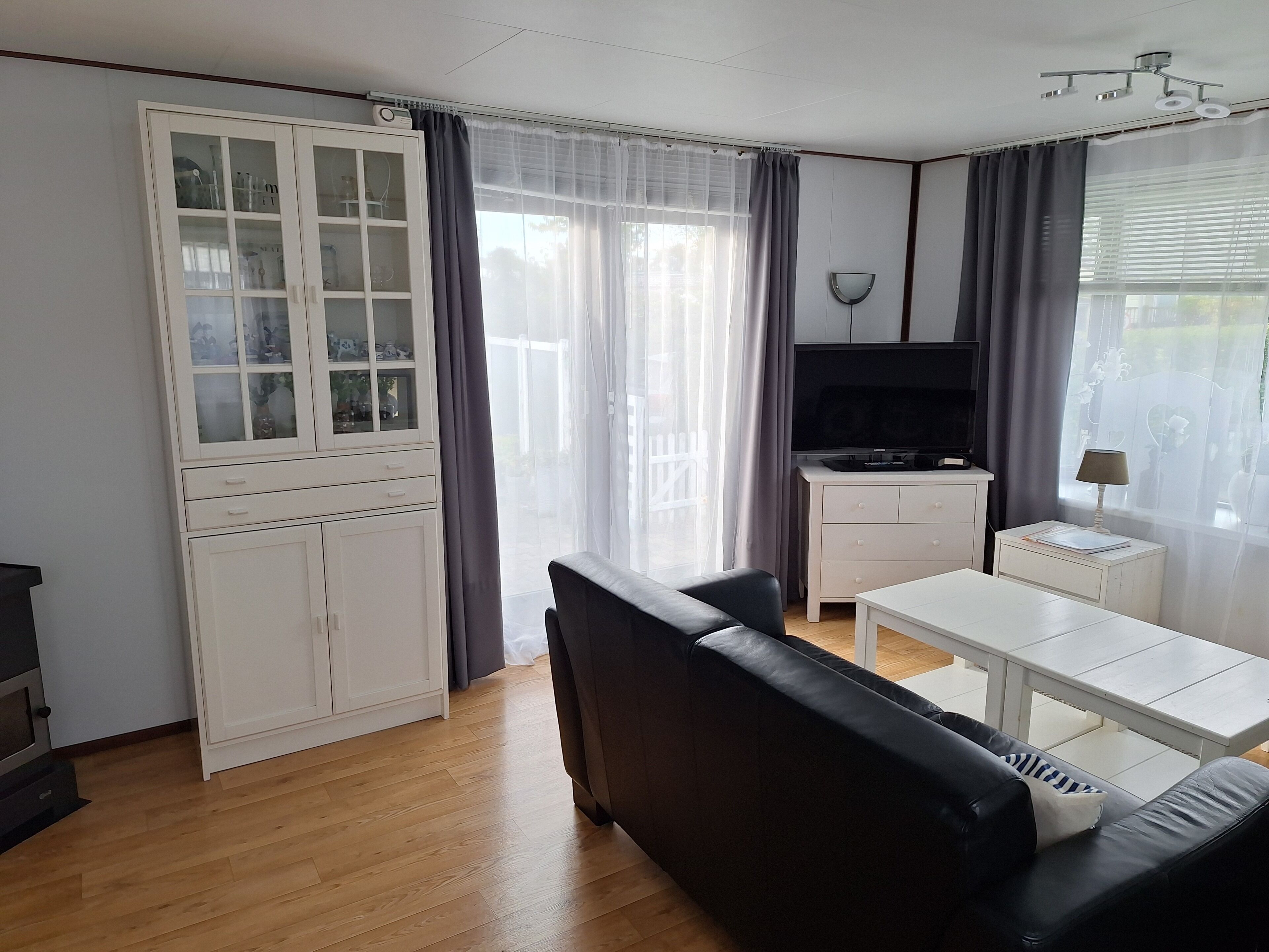 Ein modernes Wohnzimmer mit einem schwarzen Ledersofa, einer weißen TV-Konsole und einer Glasvitrine mit Dekorationselementen.