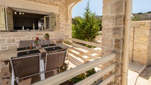 Eine Steinterrasse mit Tisch und Stühlen, ein kleiner Grill und Blick auf die umliegende Landschaft.