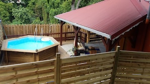 Une terrasse en bois avec un jacuzzi, un espace salon couvert et une piscine clôturée.