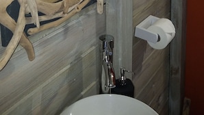 Une salle de bain avec un mur en bois, un lavabo blanc et un miroir doté d’un cadre en bois original.
