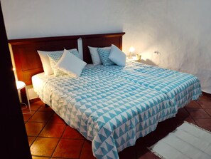 A neatly made bed with a geometric patterned bedspread, a wooden headboard, and a bedside lamp.