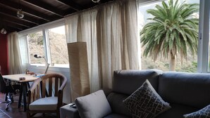 Ein Wohnzimmer mit einer Couch, einem Sessel, einem Tisch und Blick auf Palmen draußen.