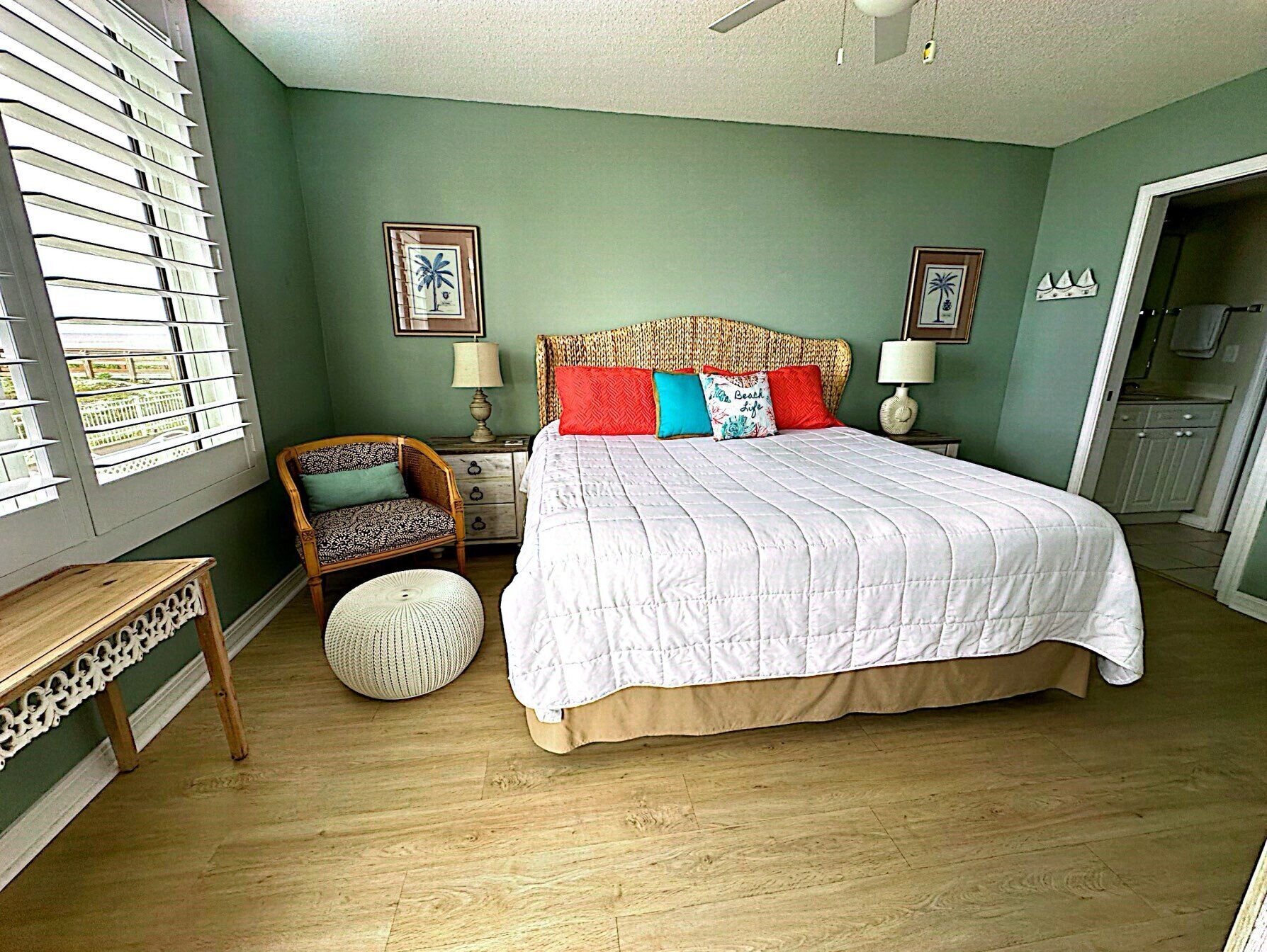 A bedroom with a large bed, a chair, a bedside table, and a window with blinds.