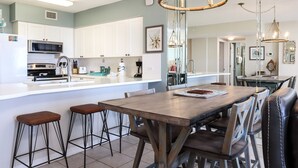 A modern kitchen with white cabinets, a central island, and a dining area with a wooden table and chairs. - Island Princess 204-Updated Beachfront with FAST Internet-Free Beach Service (Fort Walton Beach)