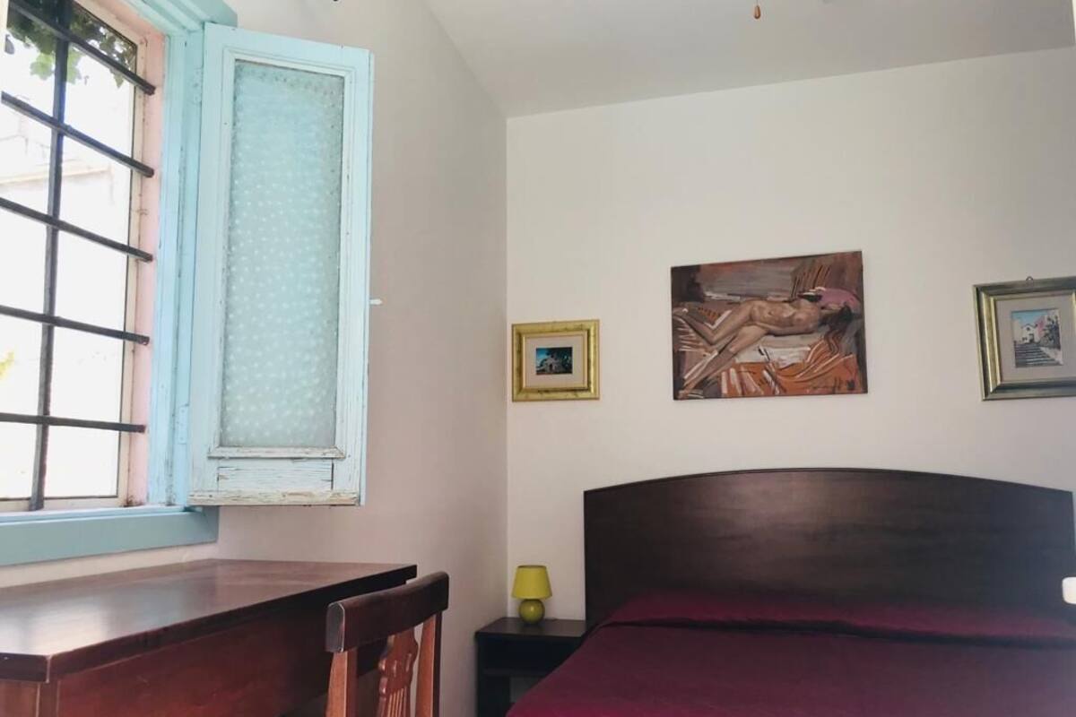 A bedroom with a wooden bed, a window with a blue frame, and two framed pictures on the wall.