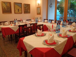 Comedor con mesas dispuestas para una comida, con manteles rojos y cubertería.