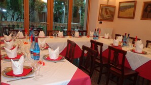 Un restaurante con varias mesas dispuestas para comer, con manteles blancos y servilletas rojas.