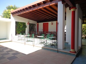 An outdoor patio with green metal chairs and tables, red columns, and a wooden pergola. - Palazzo Ricordi (Ugento)