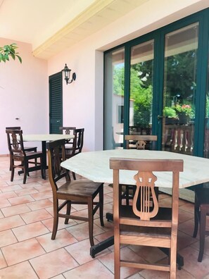 A patio with a table and chairs, a hanging plant, and a view of greenery through a glass door. - Palazzo Ricordi (Ugento)