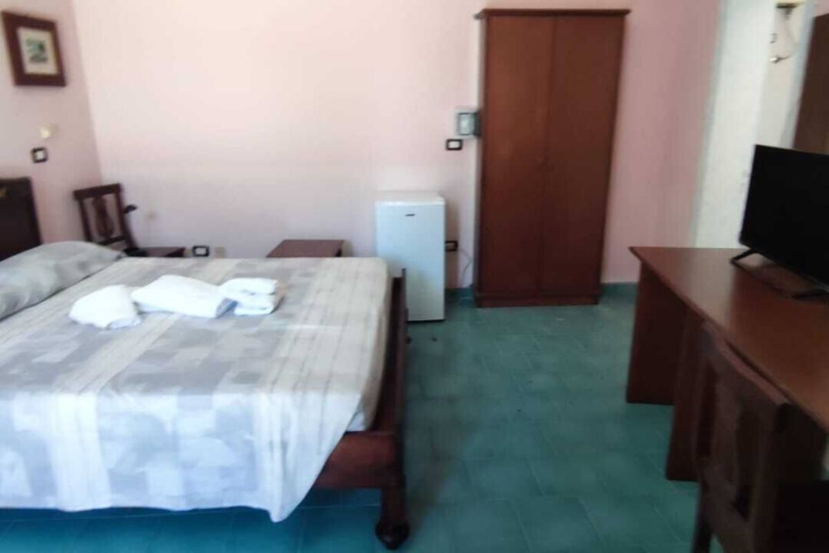 A bedroom with a bed, a television, a wardrobe, and a small table.