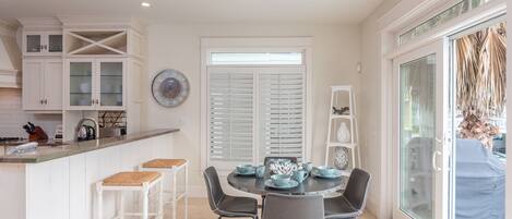 A kitchen with white cabinets, a dining table with chairs, and a window with blinds.
