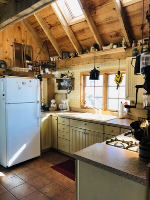 A rustic kitchen with wooden beams, a white refrigerator, a sink, and various kitchen utensils.