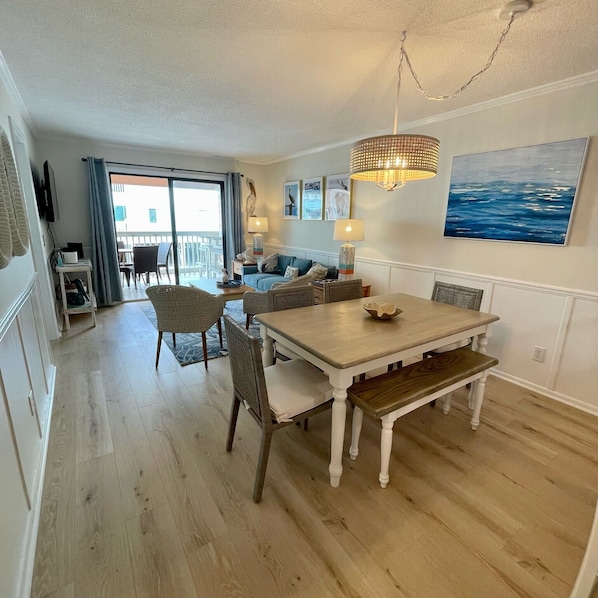 A dining area with a wooden table and chairs, a bench, and a hanging light fixture. - Duneside I 104 - Oceanfront Complex (Oceanview Unit) in Garden City Beach (Garden City)