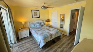A bedroom with a bed, two bedside tables, a ceiling fan, and a door leading to another room.