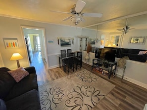 A living room with a ceiling fan, a TV, a black sofa, and a dining area with chairs and a table.