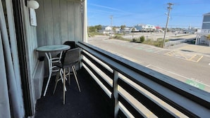 A balcony with a table and chairs, overlooking a parking lot and buildings.