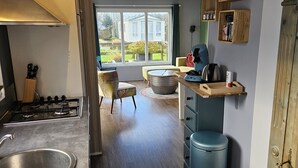 Une cuisine moderne équipée d’une cuisinière à gaz, d’un évier en acier inoxydable et de meubles de rangement en bois. On y trouve un coin repas avec une chaise et une table, ainsi qu’une grande fenêtre offrant une vue sur l’extérieur.