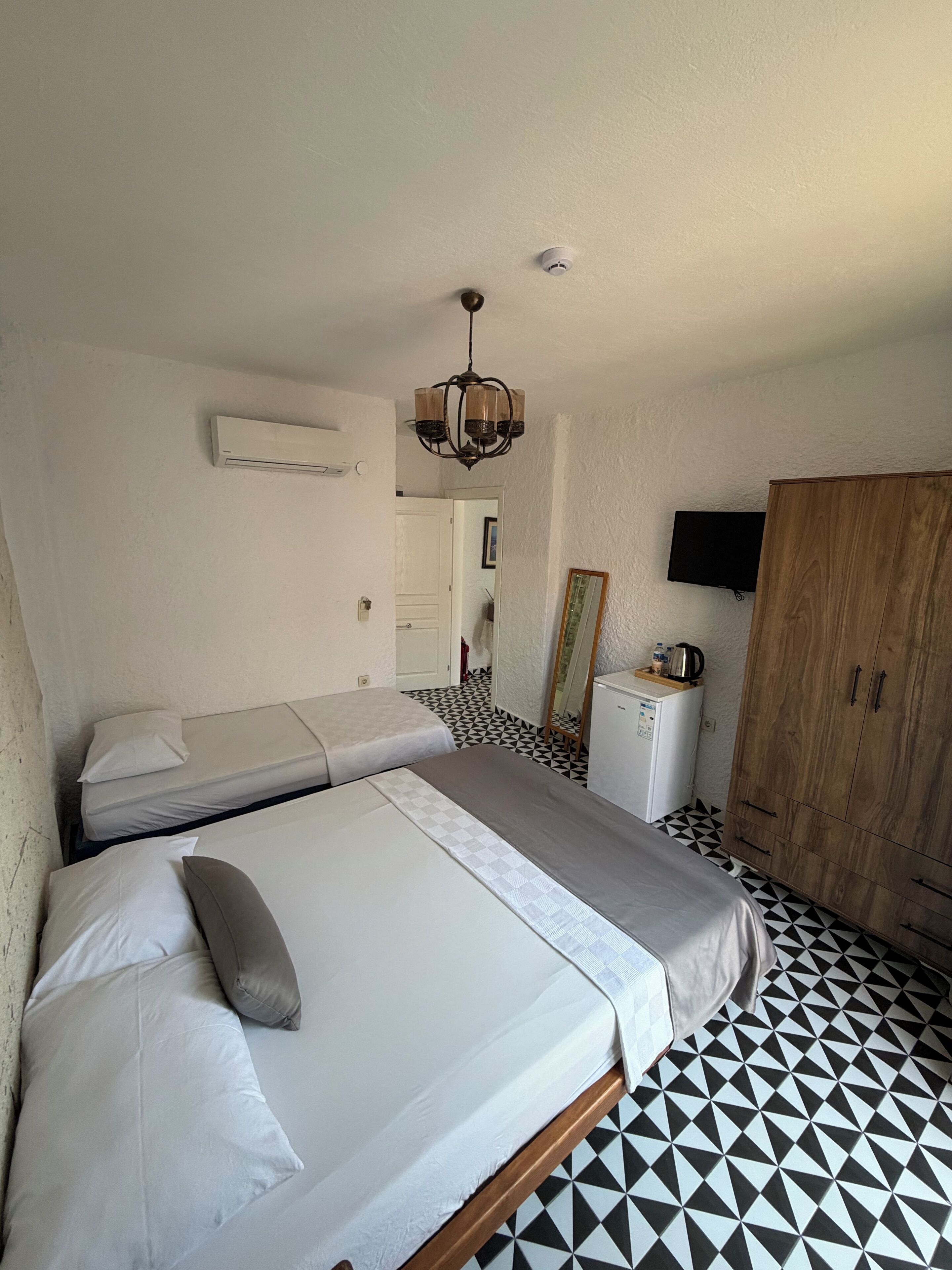 A bedroom with two beds, a wooden wardrobe, a television, and a small kitchenette.