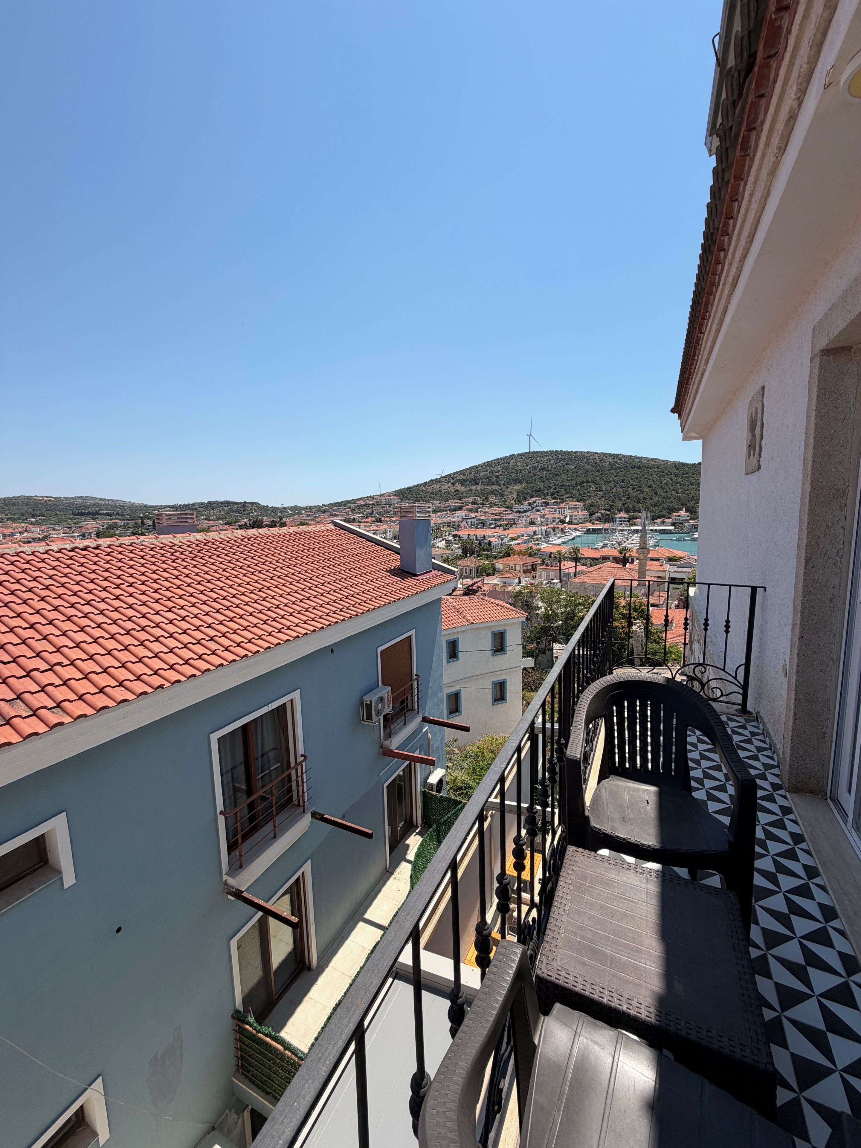 A balcony with a view of a town, a tiled roof, and a building with a window.