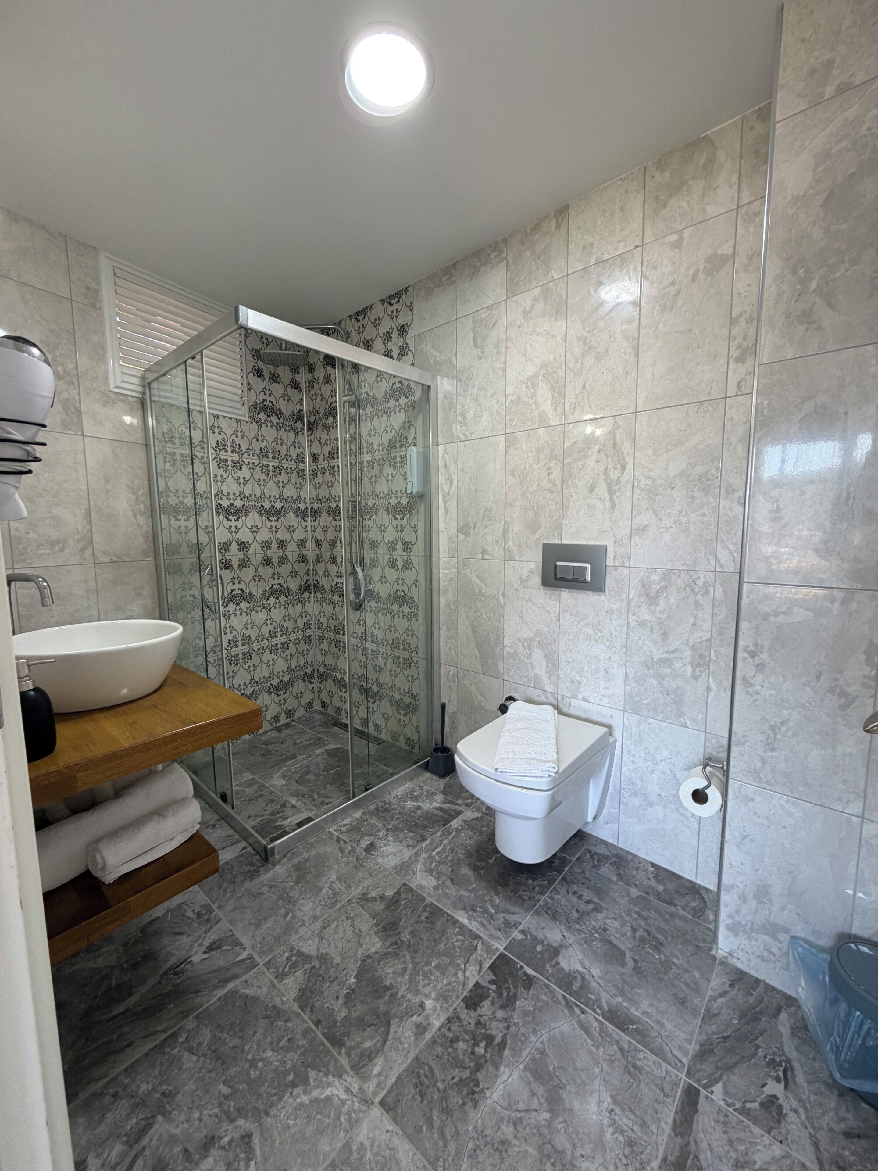 A modern bathroom with a glass-enclosed shower, a white toilet, and a sink with a wooden countertop.