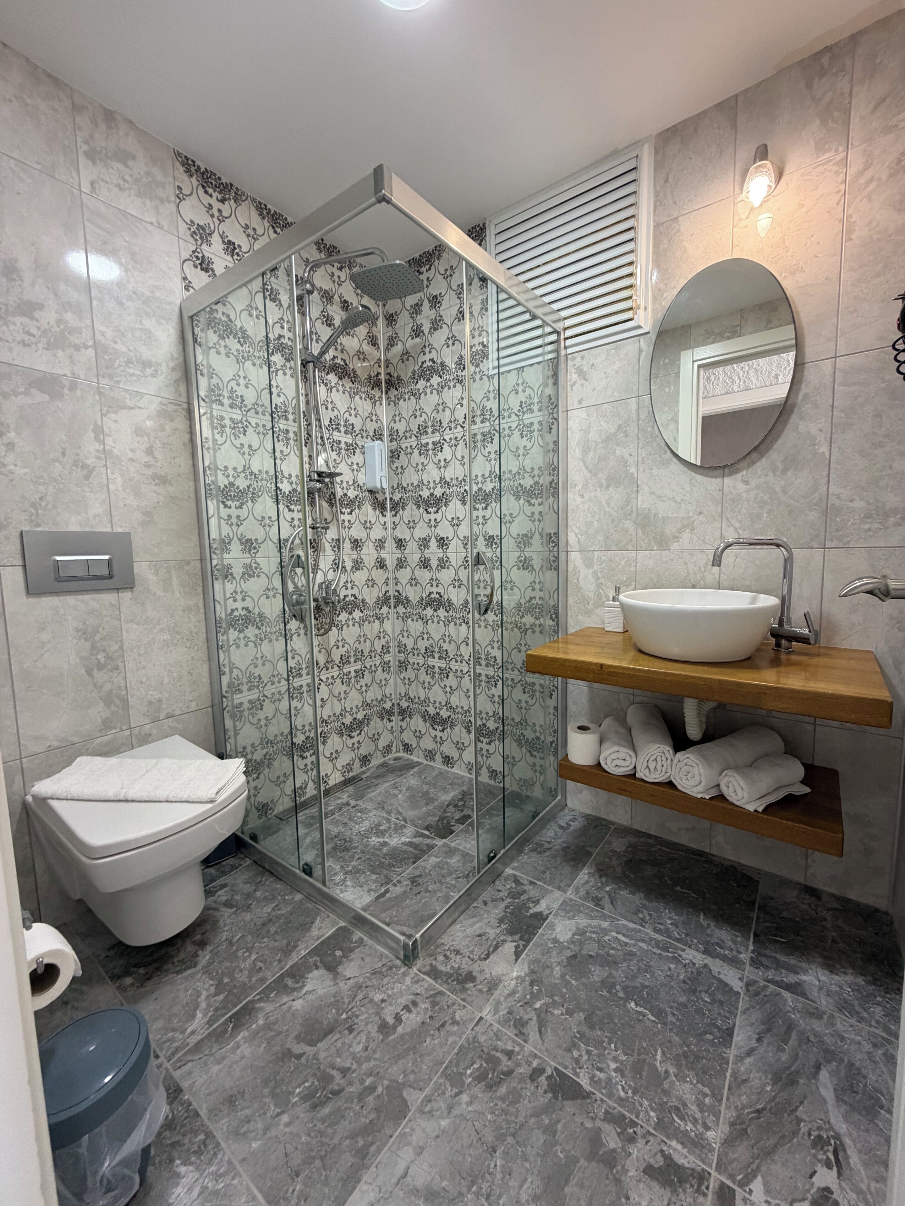 Une salle de bain moderne avec une douche à parois de verre, des toilettes, un lavabo doté d’un plan de travail en bois et un miroir.