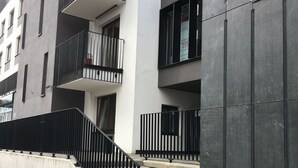 Un edificio moderno con varios balcones, una escalera que conduce a la entrada y fachada de concreto.