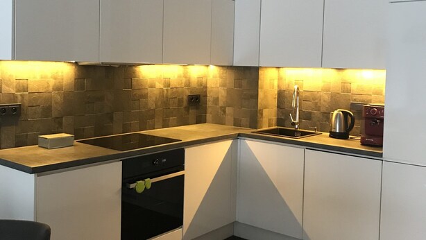 Una cocina moderna con armarios blancos, horno empotrado, lavabo y cafetera.
