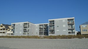 Ein mehrstöckiges Gebäude direkt am Strand mit Balkonen und einem sandigen Strand im Vordergrund.