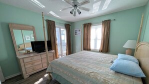 Ein Schlafzimmer mit Bett, Kommode, Fernseher, Deckenventilator und Vorhängen.