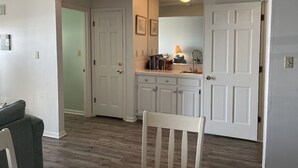 Ein Zimmer mit Esstisch, einem Stuhl, einer weißen Kommode und einer Tür zu einem weiteren Raum.