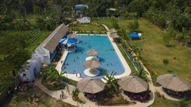 An aerial view of a resort with a central swimming pool, surrounded by thatched-roof huts and lush greenery. - Sweet Water Resort (Zamboanguita)