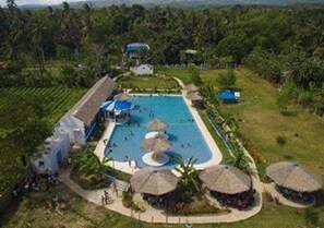 An aerial view of a resort with a central swimming pool, surrounded by thatched-roof huts and lush greenery. - Sweet Water Resort (Zamboanguita)