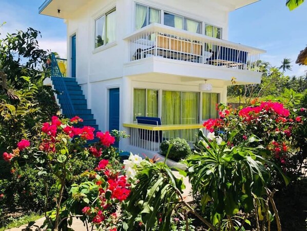 A two-story building with a balcony, surrounded by lush greenery and vibrant flowers. - Sweet Water Resort (Zamboanguita)
