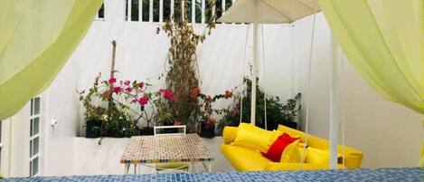 A covered outdoor seating area with a tiled table and yellow sofa.