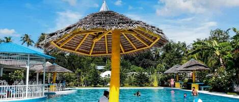 Una piscina con una sombrilla en el centro, rodeada de palmeras y un cielo despejado.