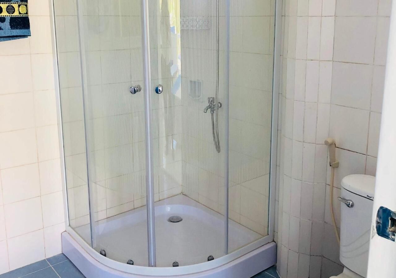 Une douche d’angle avec un pare-douche en verre et un sol carrelé de couleur blanche.
