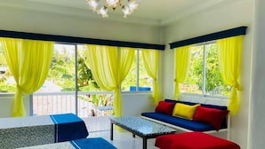 A room with a sofa, two benches, a table, and large windows with yellow curtains. - Sweet Water Resort (Zamboanguita)