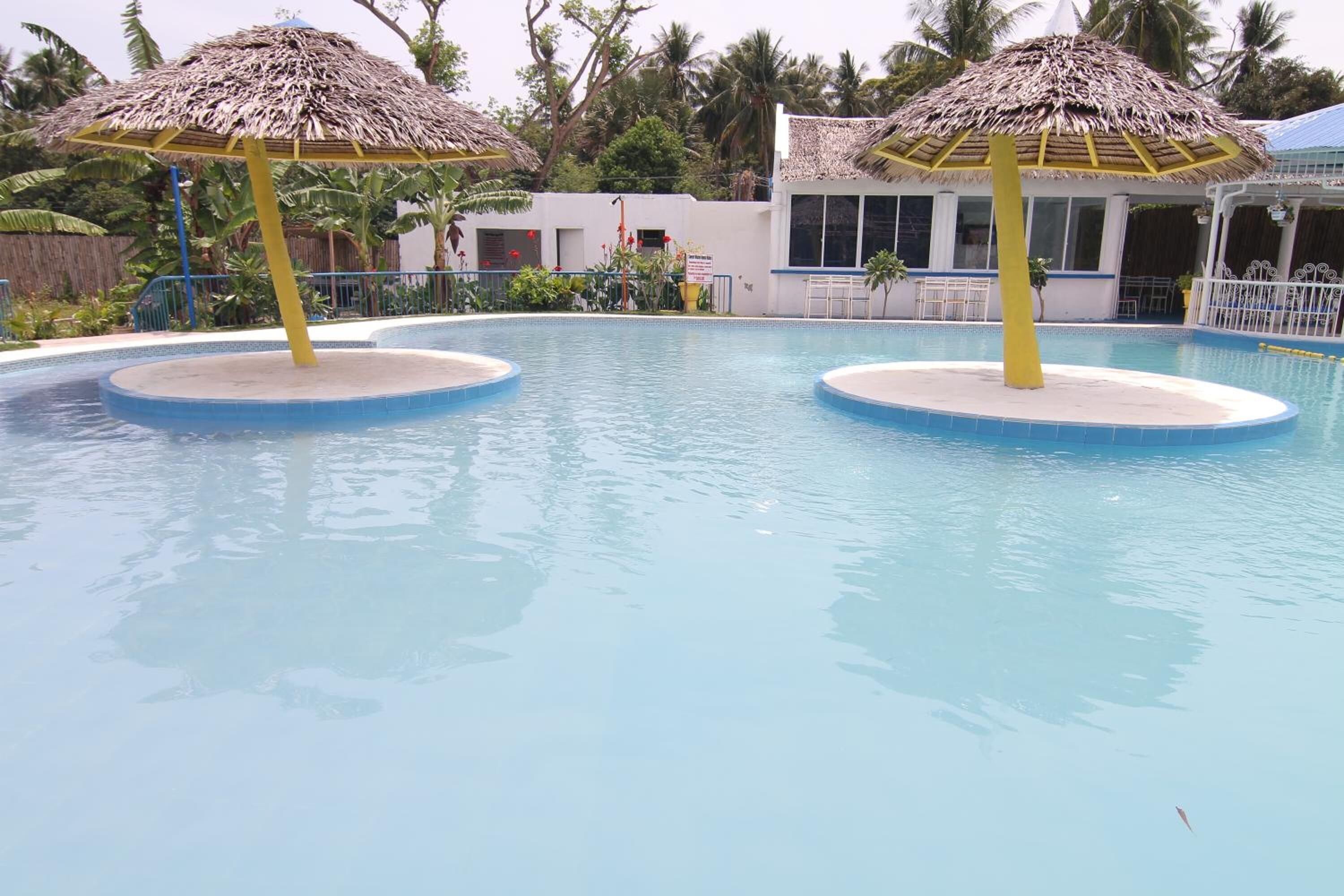 Una piscina con dos sombrillas de paja y un edificio al fondo.