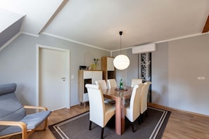 Un espace de salle à manger moderne avec une table en bois et des chaises blanches, un luminaire suspendu et un canapé gris.