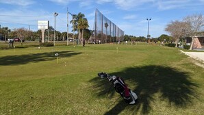 Ein Golfplatz mit blauem Himmel, einer Golftasche und einem Gebäude in der Ferne.