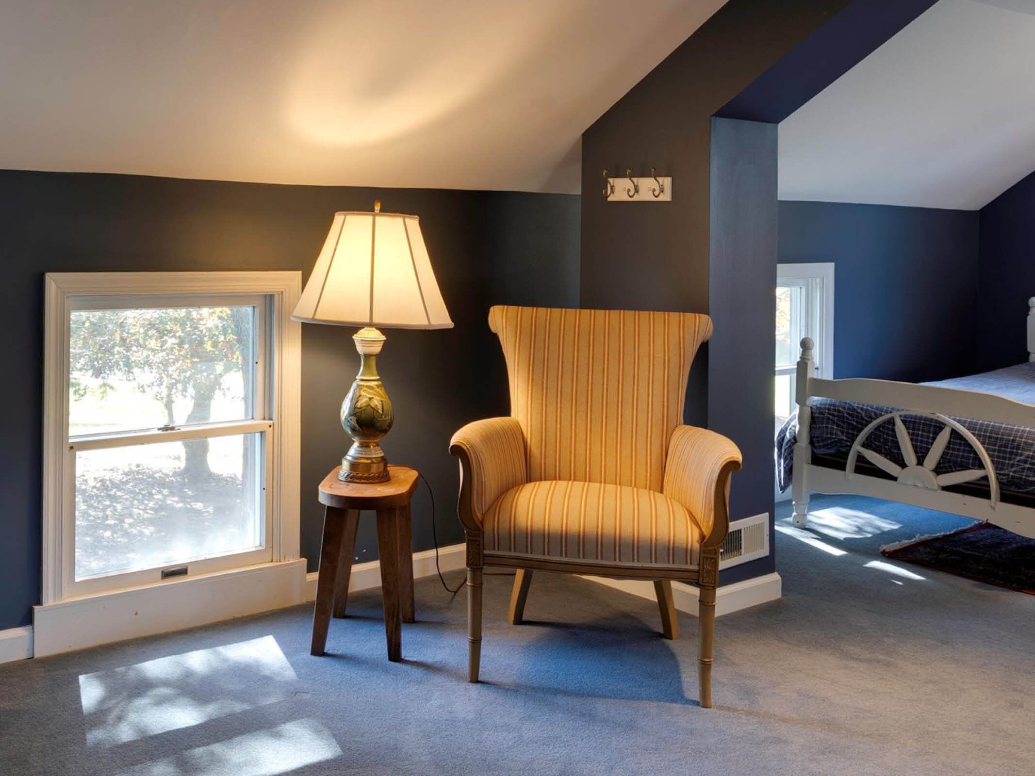 Una habitación con un ventanal grande, una lámpara, una silla y una cama.