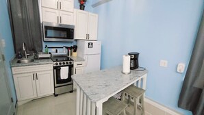 A compact kitchen with white cabinets, a microwave, a stove, and a coffee maker. - Private Studio Apartment In Lewes (Lewes)