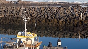 A boat docked at a rocky pier with a clear view of the surrounding landscape. - A farm in a stunning nature. Peace and quiet. Out of tourist traffic. (Dalabyggð)