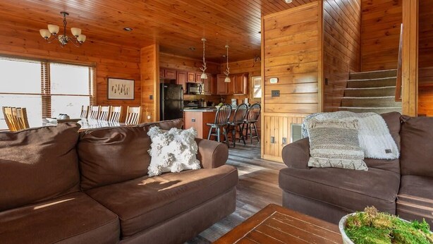A cozy cabin interior with a wooden interior, a living room with two sofas, a dining area, and a kitchen.