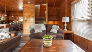 A cozy cabin interior with a wooden ceiling, a sofa set, a dining area, and a kitchen.